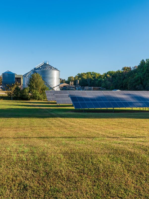 Solar panels on a grain farm with grain bins and a saw mill in the background on a sunny day in Vantown, Tennessee.